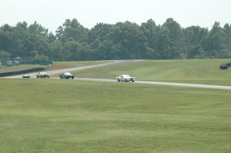 Three vintage race cars on a track, one white, one orange, one dark