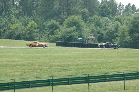 2000 Ford Mustang - Two classic Mustangs are seen on a race track, with trees and a gazebo in the background.