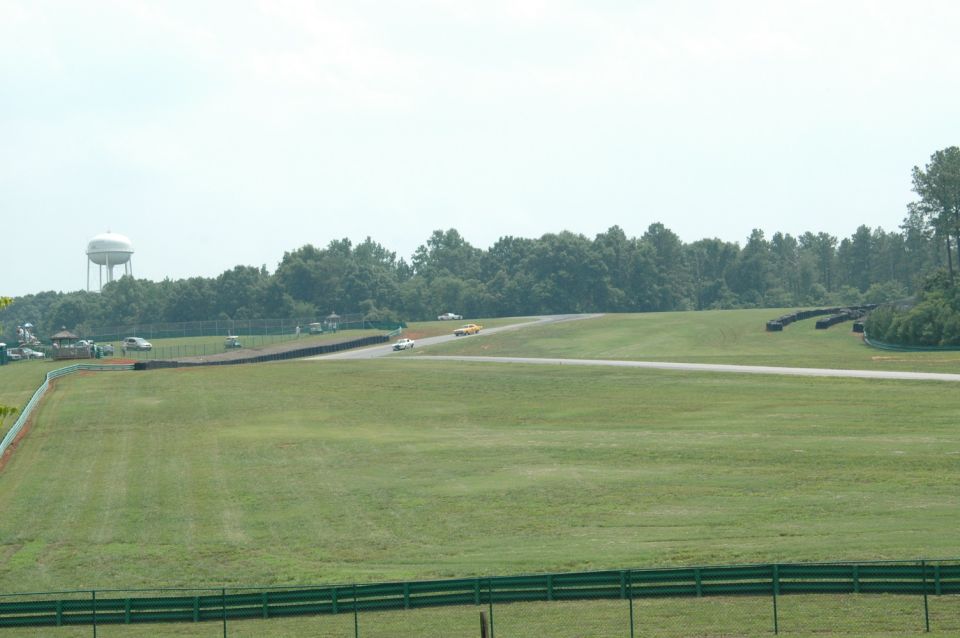 Race track with a white car and a yellow car on the track, with a water tower in the background