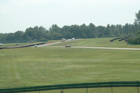 2000 Ford Mustang - Multiple cars are seen on a race track during a sunny day with trees lining the background.