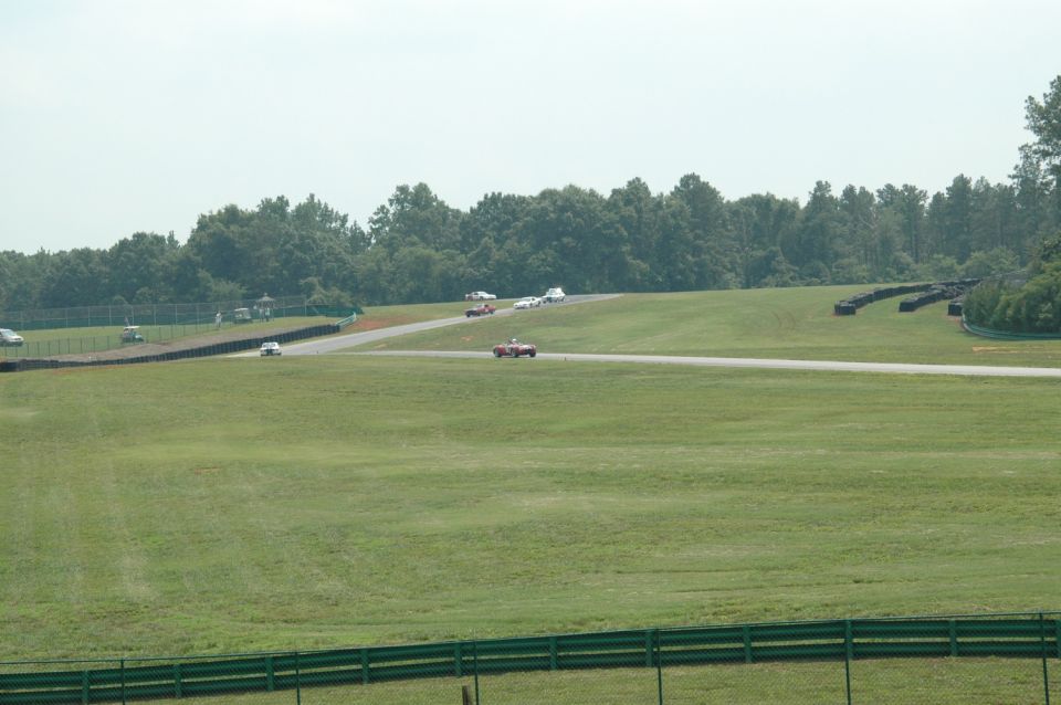 Cars on a race track with grassy infield and trees in background