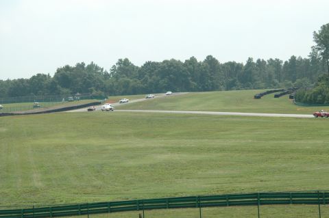 2000 Ford Mustang - Cars compete on a sunny day at a race track, with lush green scenery surrounding the course.