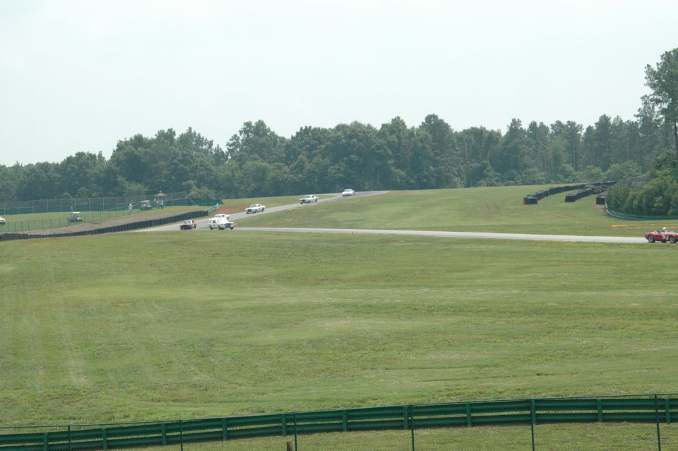 Several cars are racing on a track with green grassy hills and trees in the background
