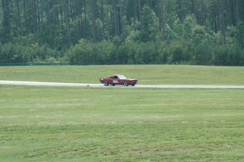 2000 Ford Mustang - A classic red Ford Mustang with racing number 550 drives on a paved track surrounded by grassy fields and trees.