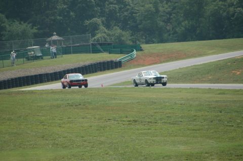 2000 Ford Mustang - Two vintage race cars compete on a track, with trees and a gazebo in the background.