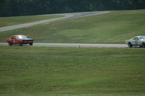 2000 Ford Mustang - A red 1969 Ford Mustang Mach 1 with a black hood races on a track, with another white car visible in the background.