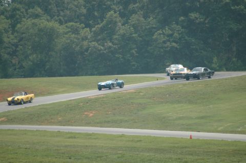 2000 Ford Mustang - A group of classic cars compete on a race track surrounded by green grass and trees.