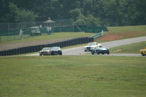 2000 Ford Mustang - A black 1965 Ford Mustang races on a track alongside other vintage vehicles.
