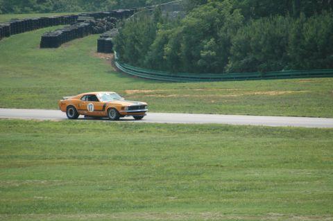 2000 Ford Mustang - A classic orange Mustang races on a track with tire barriers and trees in the background.