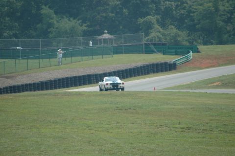 2000 Ford Mustang - A classic white 1965 Ford Mustang race car with blue stripes navigates a turn on a sunny day at a racetrack.