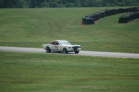 2000 Ford Mustang - A white 1965 Shelby GT350 race car, number 70, drives on a track with a grassy infield and tire barriers.