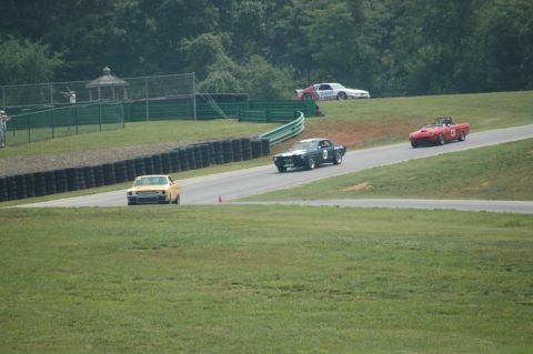 2000 Ford Mustang - Cars compete on a sunny day at a race track, with spectators visible in the distance.
