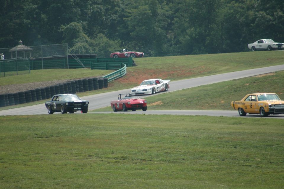 Black 1965 Ford Mustang coupe on a race track, front view, with racing decals