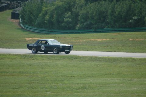 2000 Ford Mustang - A dark coupe, possibly a 1965 Mustang, races on a track with the number 84 displayed on its door.