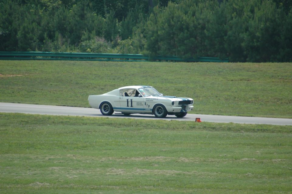 White 1960s Mustang race car with blue stripes and number 11 on the side, driving on a track