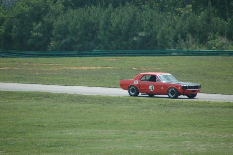 2000 Ford Mustang - A red 1967 Ford Mustang race car with a black hood and racing numbers drives on a track.