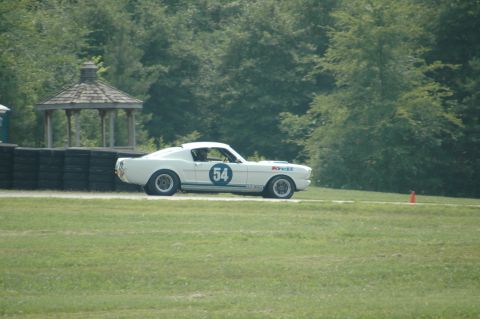 2000 Ford Mustang - A white 1960s Ford Mustang race car with blue racing stripes and the number 54 on its side drives on a track.