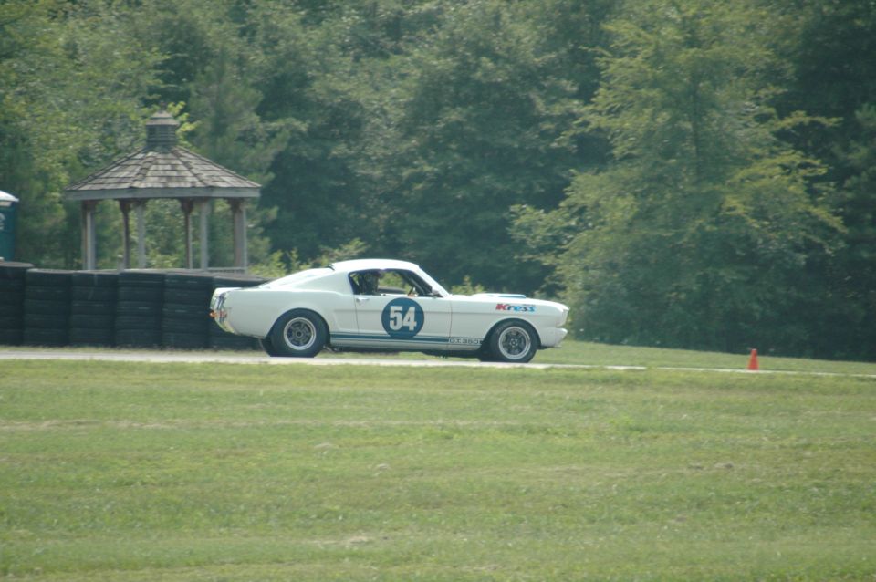 White 1960s Ford Mustang race car with blue number 54 on door, driving on a track