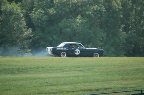 2000 Ford Mustang - A dark blue vintage Mustang coupe, possibly a 1965 model, with racing stripes and the number 84 on its side, kicks up dust on a grassy trac…