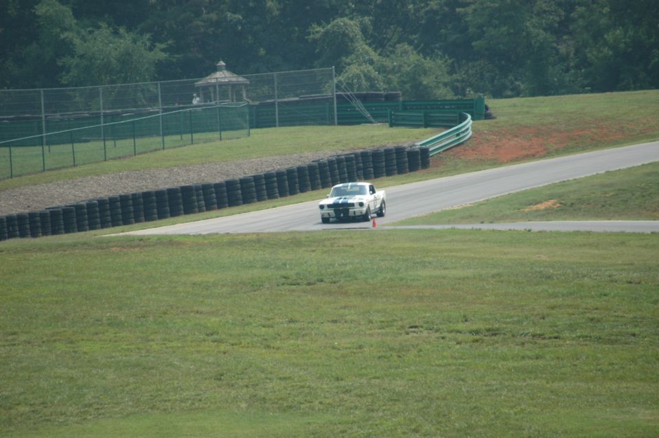 White 1967 Ford Mustang with blue stripes on a racetrack, approaching a curve