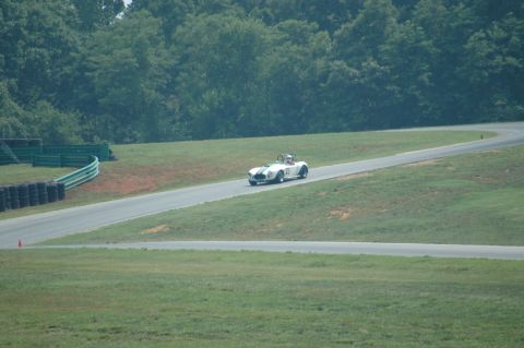 2000 Ford Mustang - A white convertible race car navigates a turn on a sunny day at a track.