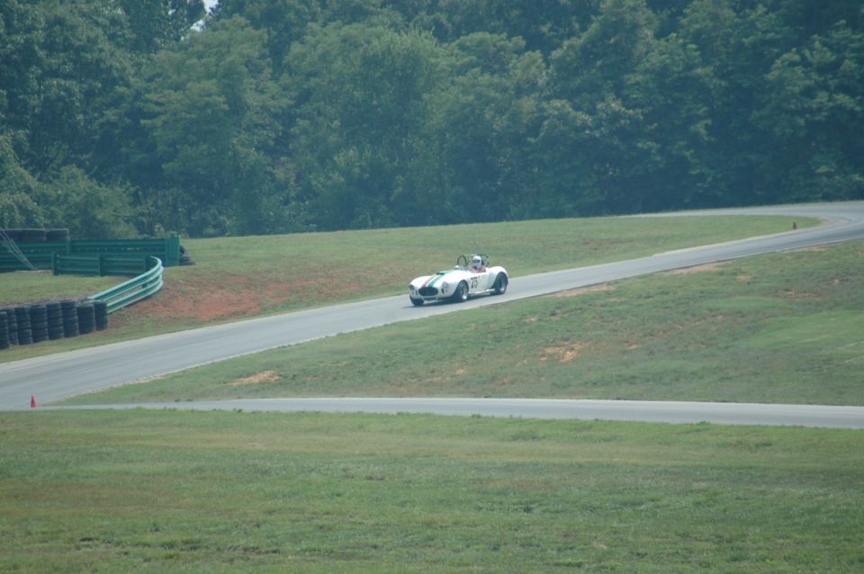 White convertible race car on a track, driver visible, trees and grass in background