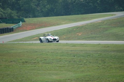 2000 Ford Mustang - A white convertible race car with red stripes drives on a paved track with grassy shoulders.