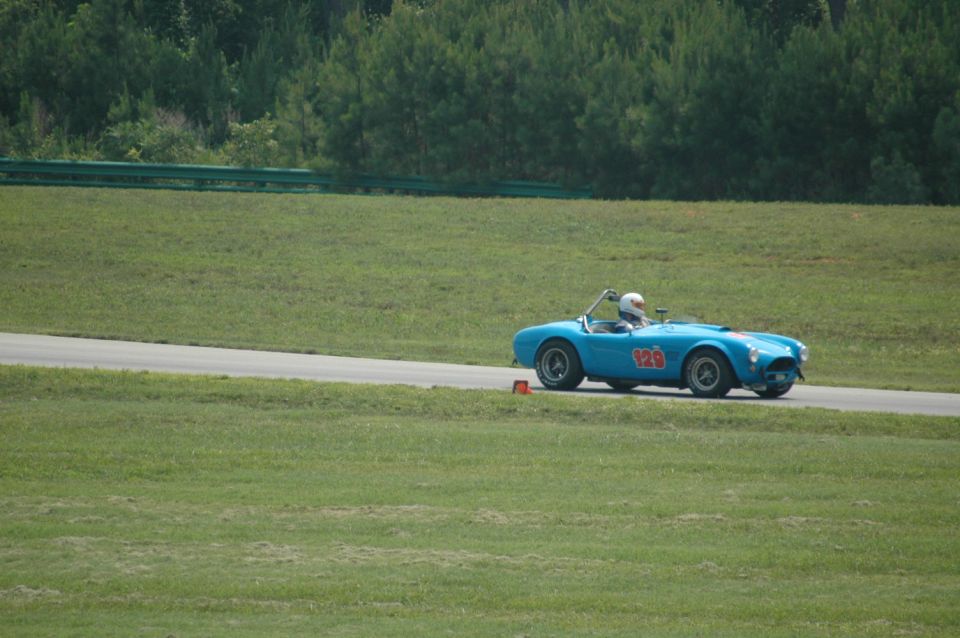 Blue convertible race car with number 129 on the side, driven by a person in a helmet on a track