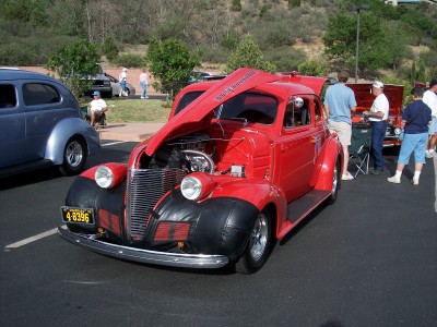 1972 Ford Ranchero - A red hot rod coupe is displayed with its hood open at an outdoor car show, with other vehicles and people around.
