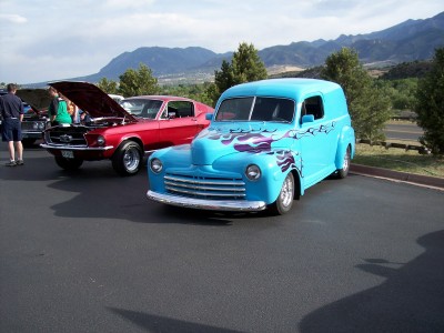 1972 Ford Ranchero - A bright blue panel van with flame graphics is parked at a car show, with a red muscle car in the background.