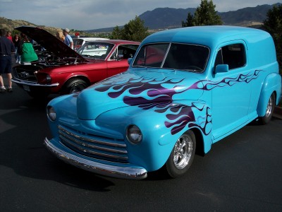 1972 Ford Ranchero - A bright blue panel van with custom flame graphics is parked next to a red car with its hood up.