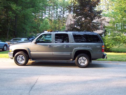 2002 Chevrolet Suburban - A gray Chevrolet Suburban is parked on the side of a road with trees and a house in the background.