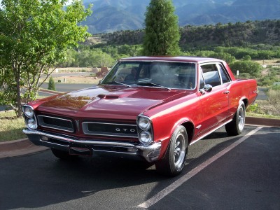 1972 Ford Ranchero - A classic red 1965 Pontiac GTO is seen parked in a lot, with a scenic mountain backdrop.