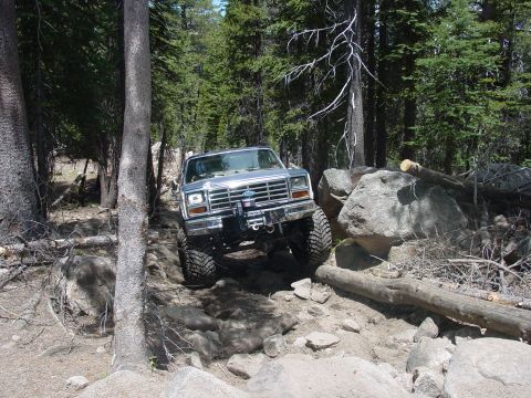 1986 Ford Bronco - This 1986 Ford Bronco is shown tackling a challenging off-road path through a wooded area.
