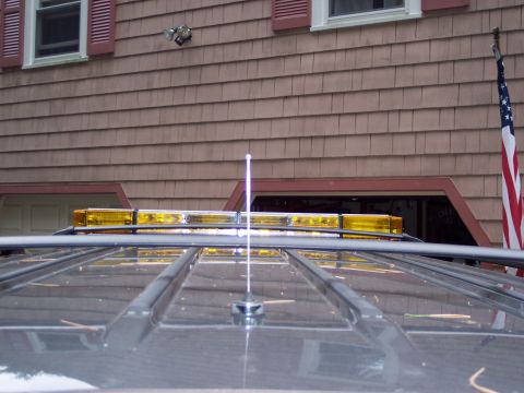 2002 Chevrolet Suburban - The top of a gray SUV is visible, equipped with a yellow light bar and an antenna, parked in front of a house.