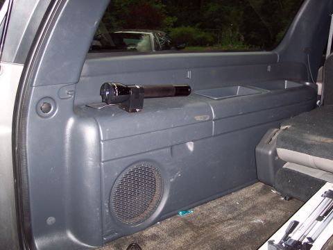 2002 Chevrolet Suburban - A flashlight rests on the storage compartment inside a vehicle, with another car visible outside.