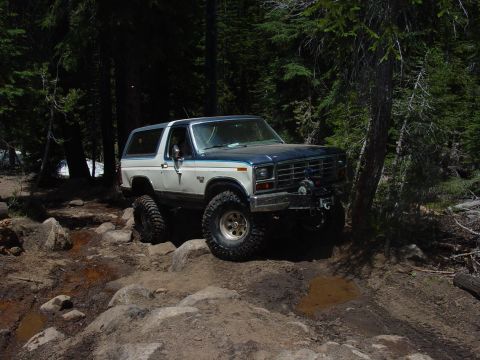 1986 Ford Bronco - This 1986 Ford Bronco is shown off-roading through a challenging, rocky path in a wooded area.
