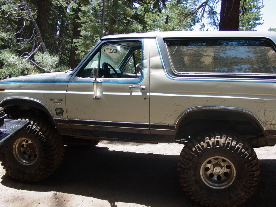 Silver and blue two-door Ford Bronco with large off-road tires, seen from the side