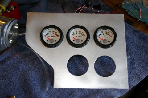 1986 Ford Bronco - A custom-cut bare aluminum gauge panel lying on a blue towel, fitted with three white-faced gauges, two oil temperature units reading 130-3…