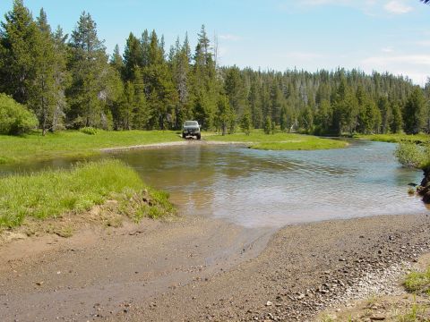 1986 Ford Bronco - Off-road vehicle navigates a river crossing in a wooded area.
