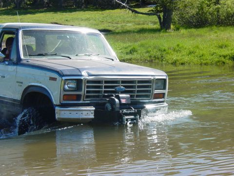 1986 Ford Bronco - Ford Bronco navigates through a water crossing on a sunny day.
