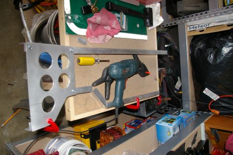 1986 Ford Bronco - A shop-fabricated aluminum panel with five drilled round gauge or switch holes clamped upright on a garage workbench, alongside a corded el…