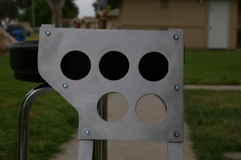 1986 Ford Bronco - A metal console with six circular cutouts and a black seat is shown in an outdoor setting.