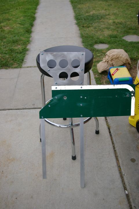 1986 Ford Bronco - A metal plate with six circular holes is attached to a stool seat, with a green panel extending from its side.