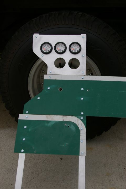 1986 Ford Bronco - A custom gauge cluster is mounted on a green panel, positioned next to a large vehicle tire.
