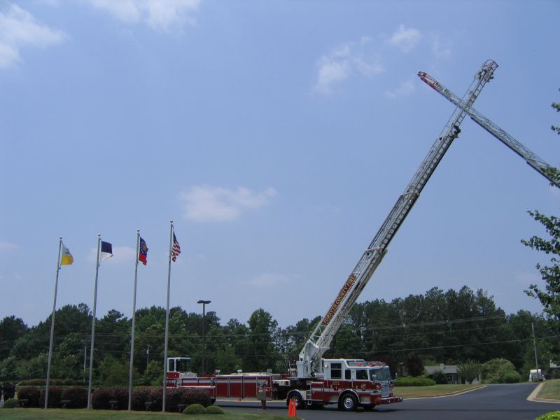 Red aerial ladder fire truck with ladder extended into blue sky beside flagpoles