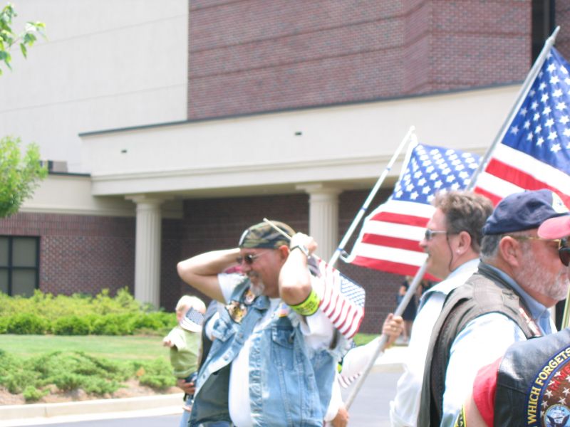 Bikers in leather and denim vests holding American flags outside a brick building