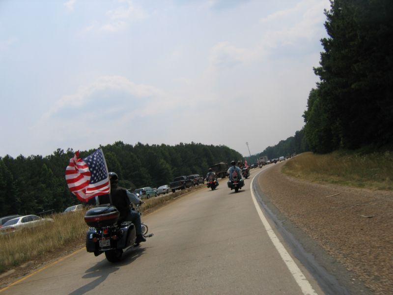 Black touring motorcycle flying a large American flag leads a group ride down a highway