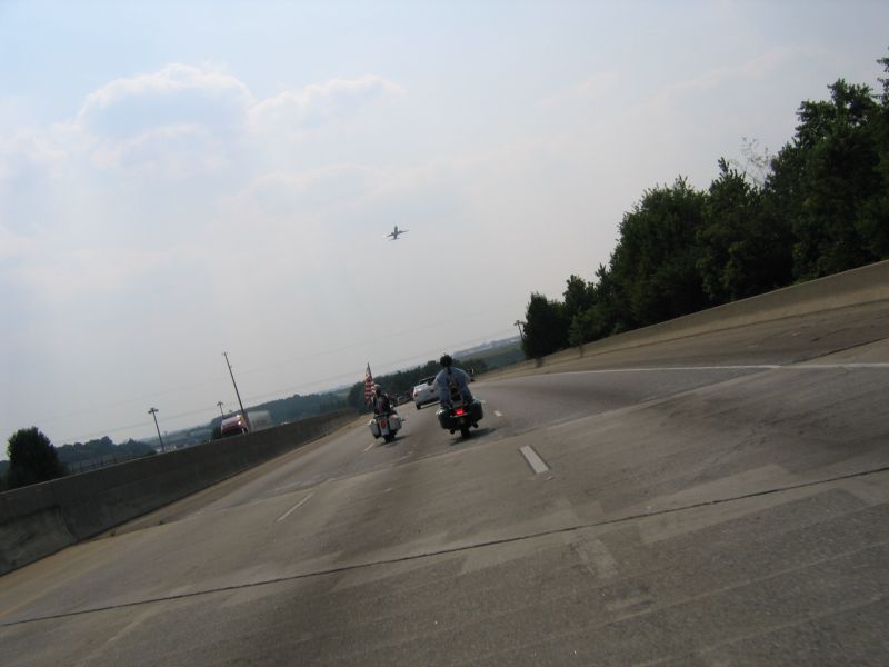 Two motorcycles riding on a highway with an airplane in the sky