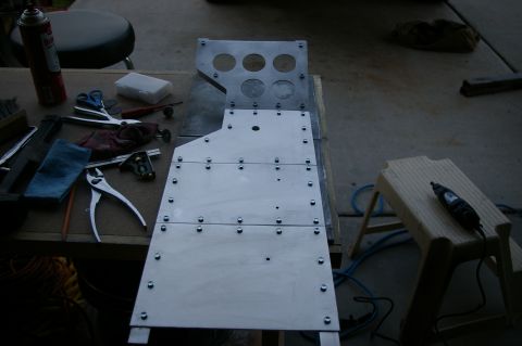 1986 Ford Bronco - A metal console part is laid out on a workbench with various tools, including pliers, scissors, and a rotary tool.